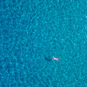 Stillness in Blue – Aerial View of Solo Swimmer in Crystal Sea